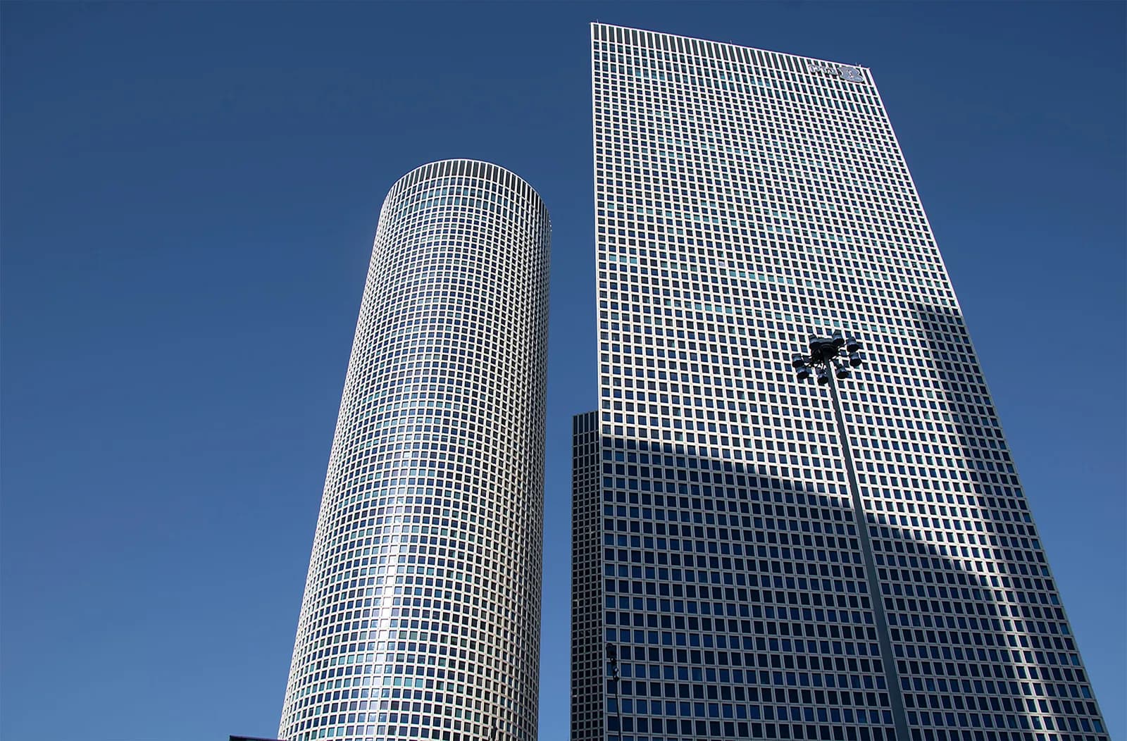 The two towers of the Azrieli Center in Tel Aviv seen from below against a clear sky