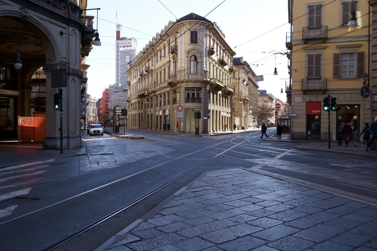 A crossing in central Turin on a winter morning: tram rails over stone paving, arcaded buildings and a corner palazzo